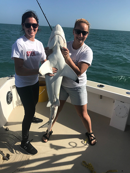 Two students holding a shark on a boat.